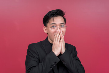 Portrait of a shocked young man wearing glasses with both hands on his mouth. Isolated on a red background.