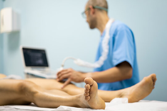 A physical therapist in a blue uniform performs an ultrasound on a patient's knee. The patient is in the foreground. Ultrasound concept in injured athletes Modern ultrasound in medical center.