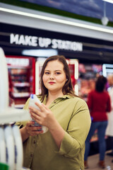 Portrait of an overweight pretty woman holding a shower gel and shopping in a store.