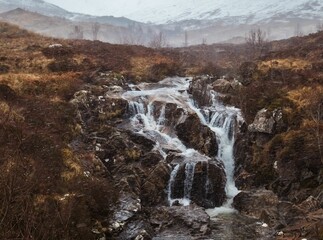 Tranquil landscape featuring a small waterfall cascading into a fast-flowing mountain stream