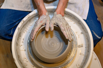 close up of ceramist woman hands working and shaping clay on the lathe or potter's wheel inside a...