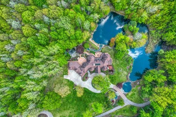 Aerial view of a big house situated in a dense forest with a tranquil lake in front of it