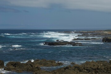 Fototapeta na wymiar Waves splashing on the rocks of the coast against the blue sky