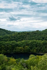 Obraz premium Vertical shot of the cloudy sky over the forested hills and a lake in spring
