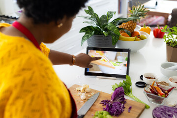 Plus size african american woman in apron preparing meal using tablet in kitchen