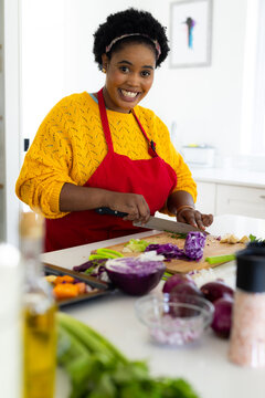 Portrait Of Happy Plus Size African American Woman In Apron Chopping Vegetables In Kitchen