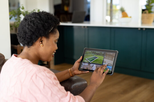 Happy plus size african american woman using tablet with home security camera views on screen