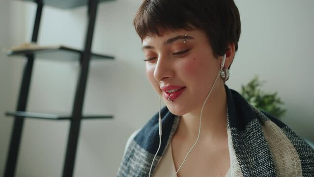 Cheerful woman with piercings talking by video call in headphones at home