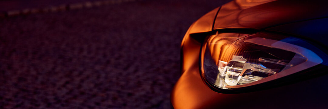 Detail of the headlight of a BMW 440i standing in the dark against the golden walls. Zory, Poland, February 19, 2023