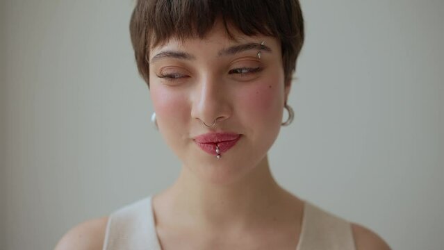 Embarrassing woman with piercings and short hairstyle looking at camera at home