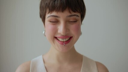 Laughing woman with piercings and short hairstyle looking at camera at home