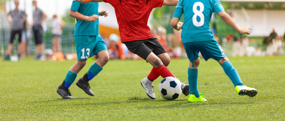 Junior competition between players running and kicking soccer. ball. Anonymous youth junior athletes in red and blue soccer shirts