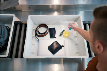 Airport security check before flight. Passenger holding plastic bag with liquids above container with personal items. .