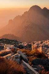 Dramatic mountain scenery and sunset haze with shining rocks and wild grasses in foreground.