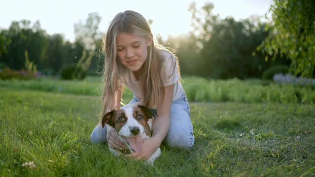 Portrait of little cute girl and pet dog walking, having fun in summer park at sunset outdoors. Little girl holding hugging favourite pedigree dog friend, Happy family kid friendship dream holiday