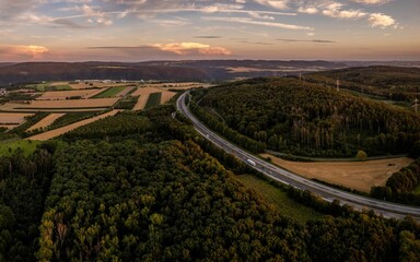 View of an orange and yellow horizon with the sun setting over a narrow road and high trees