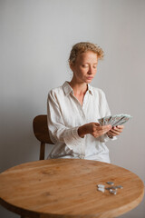 
A young student girl, of European appearance, with curly and blond hair, counts money, folding...