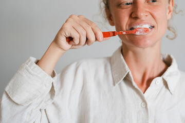 Portrait of a young girl, of European appearance, with curly hair, brushes her teeth with a red toothbrush.