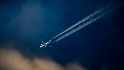 Commercial passenger aircraft flying over a blue sky, leaving a trail of contrails