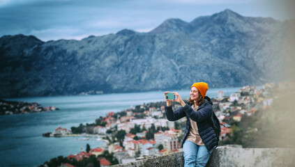 Happy woman photographs the seascapes of Montenegro using smartphone from the top of the mountain in Kotor bay