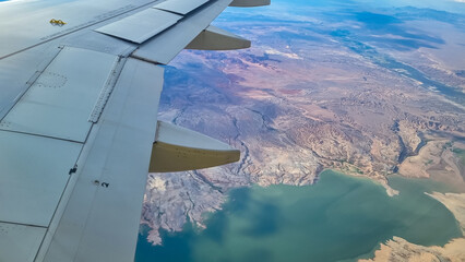 Obraz premium Flying over Nevadas canyons, deserts and lakes approaching Las Vegas, USA. A planes wing soars through the sky with breathtaking aerial birds eye view of Lake Powell Recreational Park