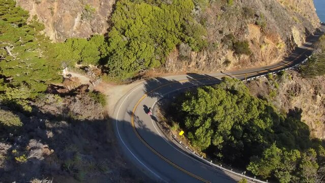 Aerial of a red motorcycle driving on the wingding road on the hillside alongside the sea
