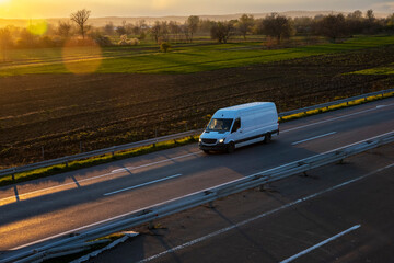 White delivery van on the highway. White modern delivery small shipment cargo courier van moving fast on motorway road to city urban suburb. The world's best transport of goods. - obrazy, fototapety, plakaty