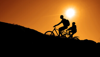Fototapeta na wymiar Silhouette of a two person riding a mountain bike uphill. beautiful sunset background. 2 people - daughter, father.
