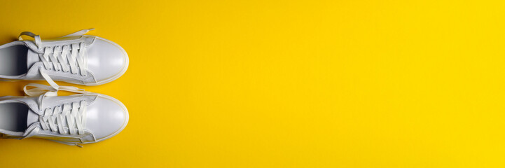 White leather shoes on a yellow background. White sneakers with white laces. New shoes. Horizontal image. Banner for insertion into site.