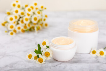 Obraz na płótnie Canvas Cream for body and hands with a chamomile flower on a light marble background. Herbal dermatological cosmetic hygiene cream. Natural cosmetic product. Cosmetic tube. Ecological cosmetics.Copy space.