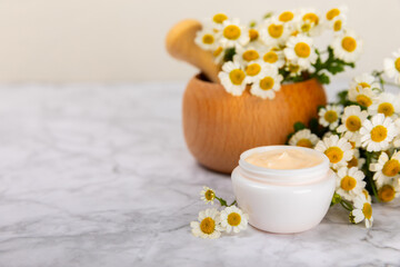 Cream for body and hands with a chamomile flower on a light marble background. Herbal dermatological cosmetic hygiene cream. Natural cosmetic product. Cosmetic tube. Ecological cosmetics.Copy space.