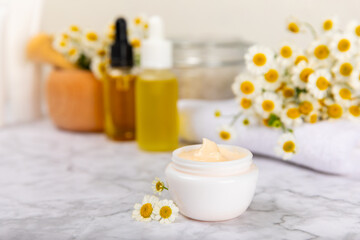 Chamomile Spa. Essential oil, sea salt, chamomile flowers, body cream and handmade soap. Natural herbal cosmetics with chamomile flowers on a textured background.Beauty concept. Cosmetic tube. 