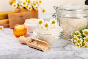 Obraz na płótnie Canvas Chamomile Spa. Essential oil, sea salt, chamomile flowers, body cream and handmade soap. Natural herbal cosmetics with chamomile flowers on a textured background.Beauty concept. Cosmetic tube. 