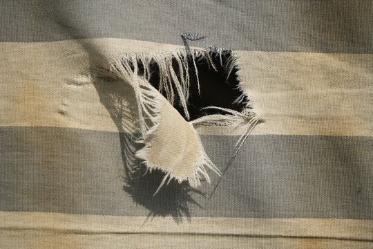 hanging teared rag spread isolated on black background , can use like a background or any texture. hole in the tissue. Unbleached beige fabric with torn stitch, hole and loose threads