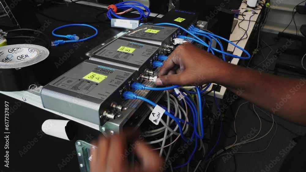 Poster slow revealing shot of a software engineers hands plugging cables into the back of a switcher unit
