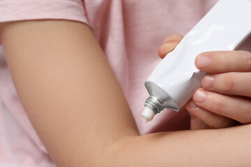 Little girl applying ointment onto her arm, closeup
