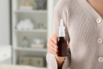 Woman holding nasal spray indoors, closeup. Space for text