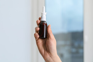 Woman holding nasal spray bottle indoors, closeup