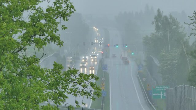 Heavy rain and slow car traffic on DK1 national road with information board in direction of Bielsko - Biała, Cieszyn in Poland. Above view with trees with green leaves around road - real time.