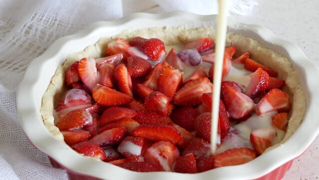 Pouring the filling over and around the strawberries in the shortbread shell, selective focus. Cooking of the Strawberry pie