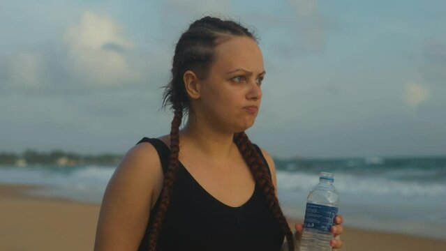 Female boxer MMA fighter girl drinking and spitting bottled water on beach.