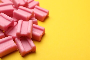 Tasty pink chewing gums on yellow background, closeup. Space for text