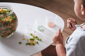 Little boy toddler sorting dry colorful pasta, learning and exploring sense of touch