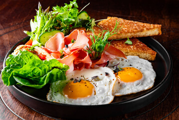 fried eggs with ham, salad and hummus on plate