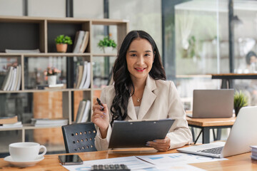 Cheerful business lady working on laptop in office, Asian happy beautiful businesswoman work in workplace. Attractive female employee office worker smile