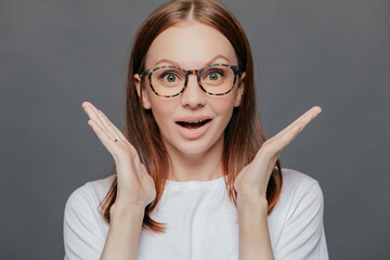 Surprised woman, pleasant appearance, palms near face. Mouth open in wonder. Casual t-shirt. Isolated on grey.