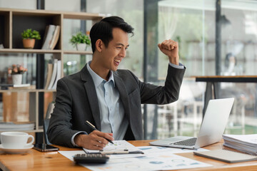 Excited business man celebrating success, reading good news in email, happy overjoyed businessman looking at laptop screen, showing yes gesture and laughing, sitting at work desk