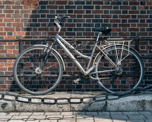 Fototapeta na wymiar Authentic old bicycle with traces of rust in the sunlight against the background of a medieval brick stone wall behind a vintage metal chain in the foreground, the shadow of the chain in foreground