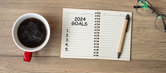 2024 GOAL with notebook, black coffee cup and pen on wood table, Top view and copy space. Happy New...