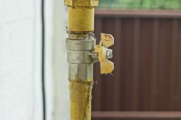part of a gas yellow color metal pipe with a closed iron ball valve near a white wall on the street during the day